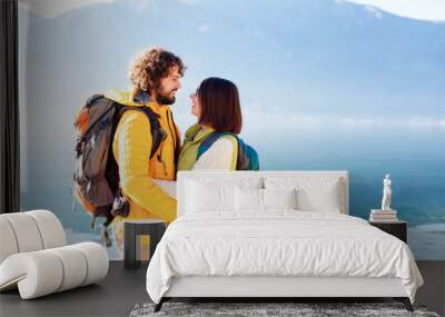 Travelers with hiking backpacks at winter sea beach. Young couple in love hugging and smiling by mountains and blue lake. Happy man and woman in vacation, adventure. Lifestyle moment. Copy space Wall mural