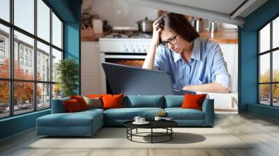 Upset woman working from home office. Unhappy freelancer using laptop and the Internet. Workplace in cozy kitchen. Concept of female business and career, housekeeping, stress. Lifestyle moment. Wall mural