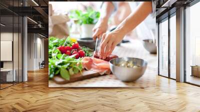 Woman is cooking in home kitchen. Female hands cut salami, vegetables, greens, tomatoes on table on wooden boards. Ingredients for preparing italian or french food. Lifestyle moment. Wall mural