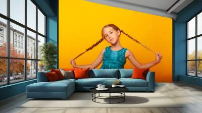 a little girl holds her hands by pigtails showing fun on a yellow background Wall mural