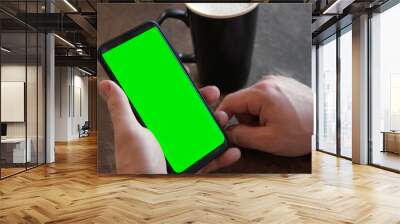 Man Use of Mobile Phone with Blank Green Screen in Cafe on Rustic Vintage Wooden Table. Male Holding Smart Phone Empty ChromaKey Screen Mock up in Coffee Shop. Morning. Showing Mock up Video Wall mural