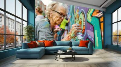 Street artist drawing graffiti, looking to the wall with her paintings. Stylish old woman, graffiti artist doing artwork outdoors. Urban Senior painter made big street art. Entertainment, subculture Wall mural