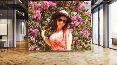 Girl in the flowers in the summer. Woman in a hat on a background of pink plants. The concept of natural beauty and youth. Natural emotions of joy. Soft focus. Hard light. Copy space Wall mural