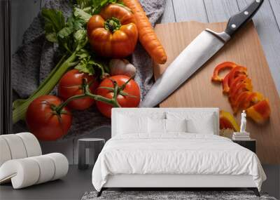 fresh vegetables on a light kitchen table. sliced paprika, orange carrot, two-tone paprika, red tomato and salad with knife on the kitchen table Wall mural