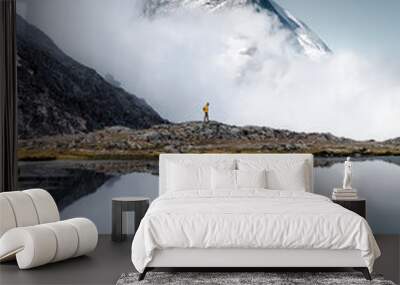 Hiker man walks alone through the incredible Swiss Alps with the Matterhorn in the background between clouds and mystery while it is reflected in the Riffelsee lake Wall mural