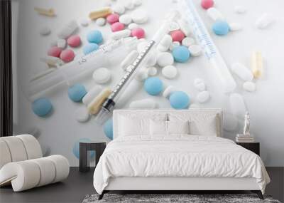 Pile of blue, white, pink and yellow colored pills and capsules with medical syringes with black and blue  markings on white background Wall mural