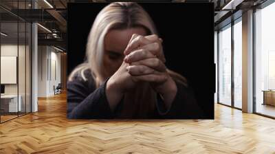 Woman praying with her hands clasped in front of her face, in dark room Wall mural