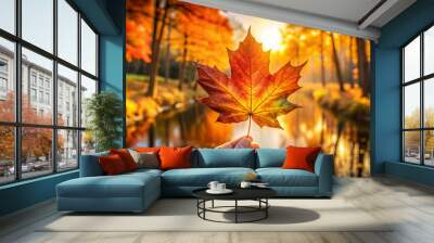 Person holding a maple leaf with joy near a tranquil autumn river background Wall mural