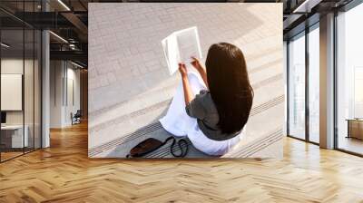 Young woman seating on stairs and reading her favourite book in a nice sunny summer day. Concept of recreation, education and study, time out Doha, curiosity, leisure time Wall mural