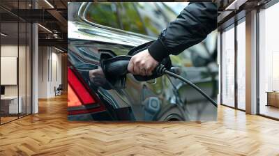 a man's hand connects an electric car to a charger Wall mural