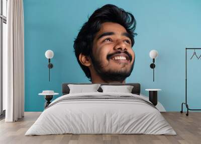 Happy joyful smiling young indian man looking a side up isolated on light blue background Wall mural