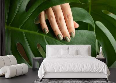 Woman's hand with a green manicure against the background of a monstera leaf Wall mural