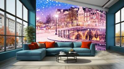 Traditional Dutch old houses and bridges on the canals in Amsterdam on a snowy winter night, The Netherlands Wall mural