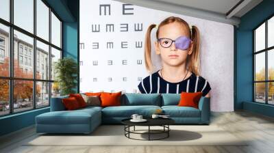 Little girl wearing glasses and eye patch or occluder with blurry eye chart at the background, amblyopia (lazy eye) treatment Wall mural