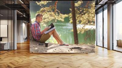 young man reading magazine outdoor with lake on background summer vacations and lifestyle concept Wall mural