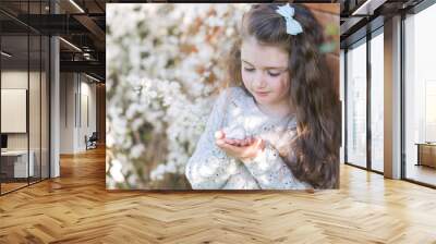 Cheerful little girl holding ceramic rabbit in her hands in front of blossoming cherry tree. Close-up Wall mural