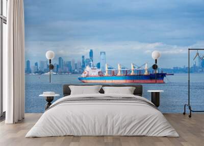 A cargo ship rests anchored in the bay, dominating the foreground. In the distance, the steel-blue skyline of New York City looms under a cloudy sky, blending into the moody, overcast atmosphere. Wall mural