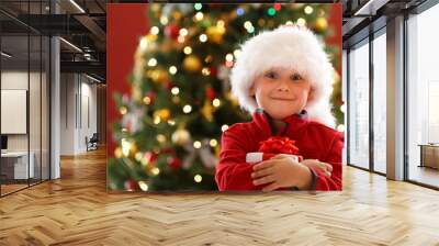 Little boy holding Christmas gift box, decorated Christmas tree on background Wall mural