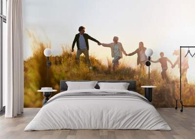 Grandpa is in the lead. Shot of a multi-generational family walking hand in hand across a field at sunset. Wall mural