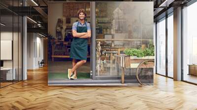 The secret to our amazing coffee lies behind these doors. Portrait of a successful young barista standing in the doorway of a coffee shop. Wall mural