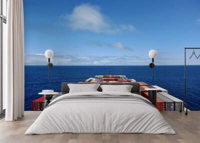 View on the containers loaded on deck of the large cargo ship. She is sailing through calm, blue ocean.  Wall mural