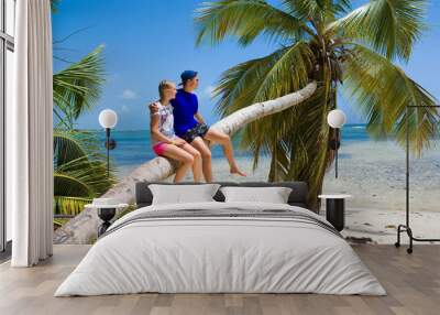 Teenagers sitting on inclined palm tree on wild coast of Sargasso sea, Punta Cana, Dominican Republic Wall mural