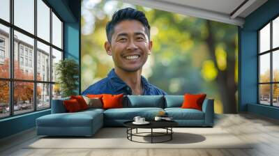 An Asian man of 40 years old smiles and looks into the distance against the background of a blurred park and sunset. a reportage frame. A smiling and optimistic person in nature. Wall mural