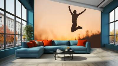 Silhouette of jumping man on sunset fiery sky background in mountain Wall mural