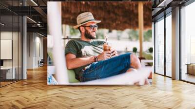 Young man drinking ice coffee in a beach bar Wall mural