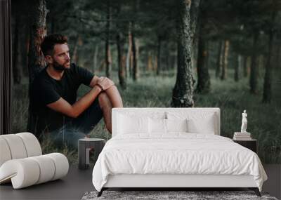 Young man sitting on grass in the woods contemplating Wall mural