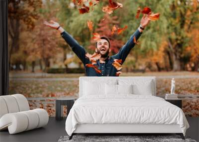 Young man throwing autumn leaves in the air Wall mural