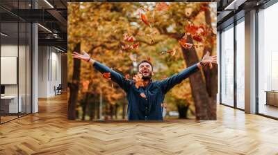 Young man throwing autumn leaves in the air Wall mural