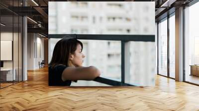 Young sad woman looking outside through balcony of an apartment building Wall mural