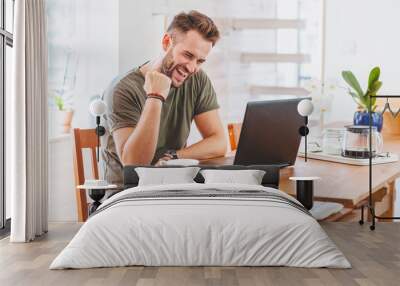 Young successful man working on laptop at home Wall mural