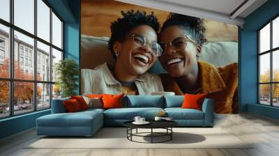 A cheerful teenage black American girl hugs her happy mother while sitting on the couch with a cup of tea Wall mural