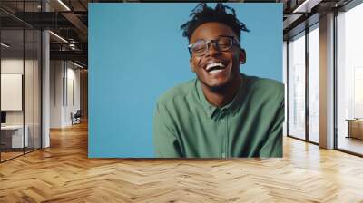 An African American teen poses on a blue studio backdrop wearing a mint shirt and yellow sunglasses Wall mural