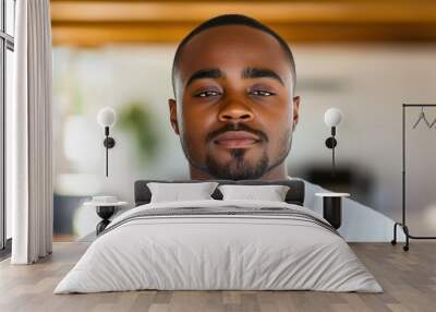 A close-up portrait of a young black man wearing a casual t-shirt, with a blurred background. Wall mural