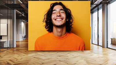 He is a Hispanic man in his 20s wearing an orange casual shirt and a yellow color background. This is a portrait depicting sincere emotions and lifestyle concept. Wall mural