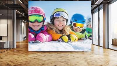 In the snow, a group of ski class children enjoy the view, smiling and looking at the camera as they lay together beside the mountain. Wall mural