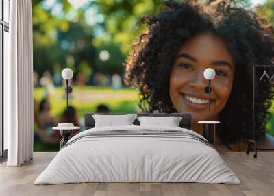 Towards the background is a blurry image of young smiling woman with curly hair wearing blue t-shirt, posing for the camera in the park. Pictured on a summer day, she is out with her friends enjoying Wall mural