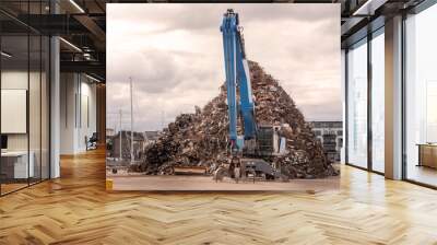 Blue excavator with claw arm in a scrap metal yard. Metal recycling industry. Export of junk for profit and ecology. Port area. Wall mural