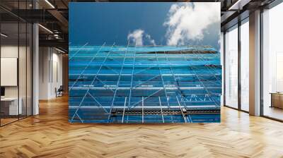 Building in scaffolding and blue mesh net matching blue cloudy sky. Construction and renovation industry in town. Wall mural