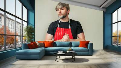 Butcher in black shirt and classic red and white stripe apron on light color background. Model in 40s with grey beard and hair. Meat industry worker. Wall mural