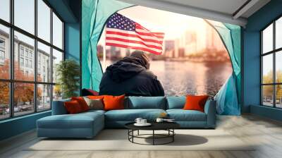 Homeless man hands on his head in despair wearing dark cloths in a tent, USA flag and beautiful city down town at sunrise. Financial problems and social issue. Losing hope to change your life concept. Wall mural