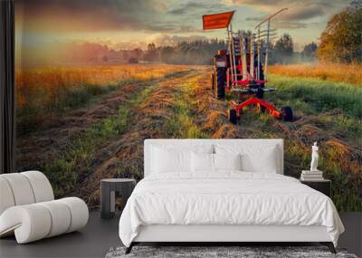 Old rusty tractor with grass cutting machine in a agriculture field with tall grass at stunning sunrise. Farming industry. Beautiful nature scene at special time. Nobody. Wall mural