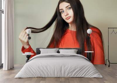 Portrait of a young teenager girl in red shirt on light color background. Model holding her long luxurious hairs. Beauty and fashion concept. Calm face expression. Wall mural