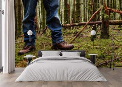 Tourist in blue jeans and tough brown leather outdoor boots on a green moss in a dense forest. Trip to nature and outdoor activity concept. Wall mural