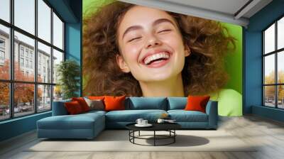 A joyful girl with curly hair smiles brightly against a vibrant green background, showcasing happiness and positivity. Wall mural