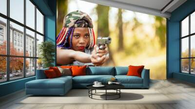 Portrait of a beautiful young African American girl with a dreadna haircut with a gun in her hands. she aims at the attacker. photo self defense concept Wall mural