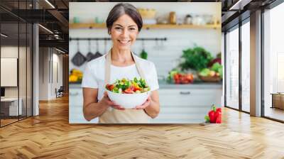  Aged woman smiling happily and holding a healthy vegetable salad bowl on blurred kitchen background, with copy space  Wall mural